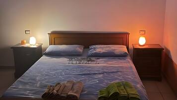 A bedroom with a bed, two bedside tables with lamps, a nightstand, and a wall-mounted light fixture.
