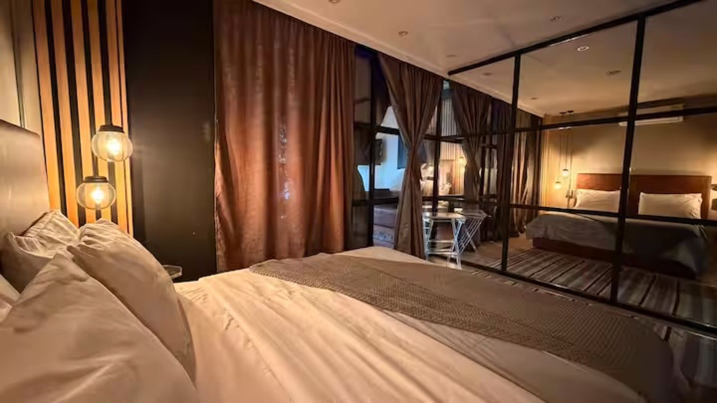 A hotel room with a large bed, a desk, and a view through a glass partition.