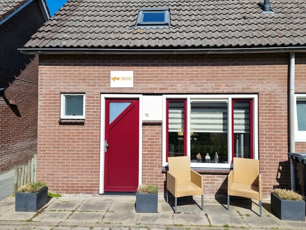 A two-story brick building with a red door, numbered 71, and two wicker chairs outside. - Do15 Holiday Home Domburg (Domburg)