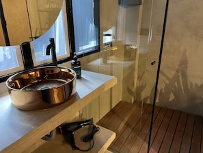 Casa de banho com uma grande bacia de cobre, secador de cabelo manual e um frasco de sabonete líquido sobre bancada de madeira.
