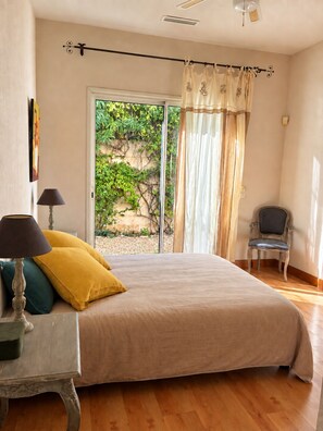 A bedroom with a bed, a chair, a table, and a view of greenery outside. - Villa Riviera Sainte-Maxime – Panoramic view of the Bay of Saint-Tropez (Sainte-Maxime)