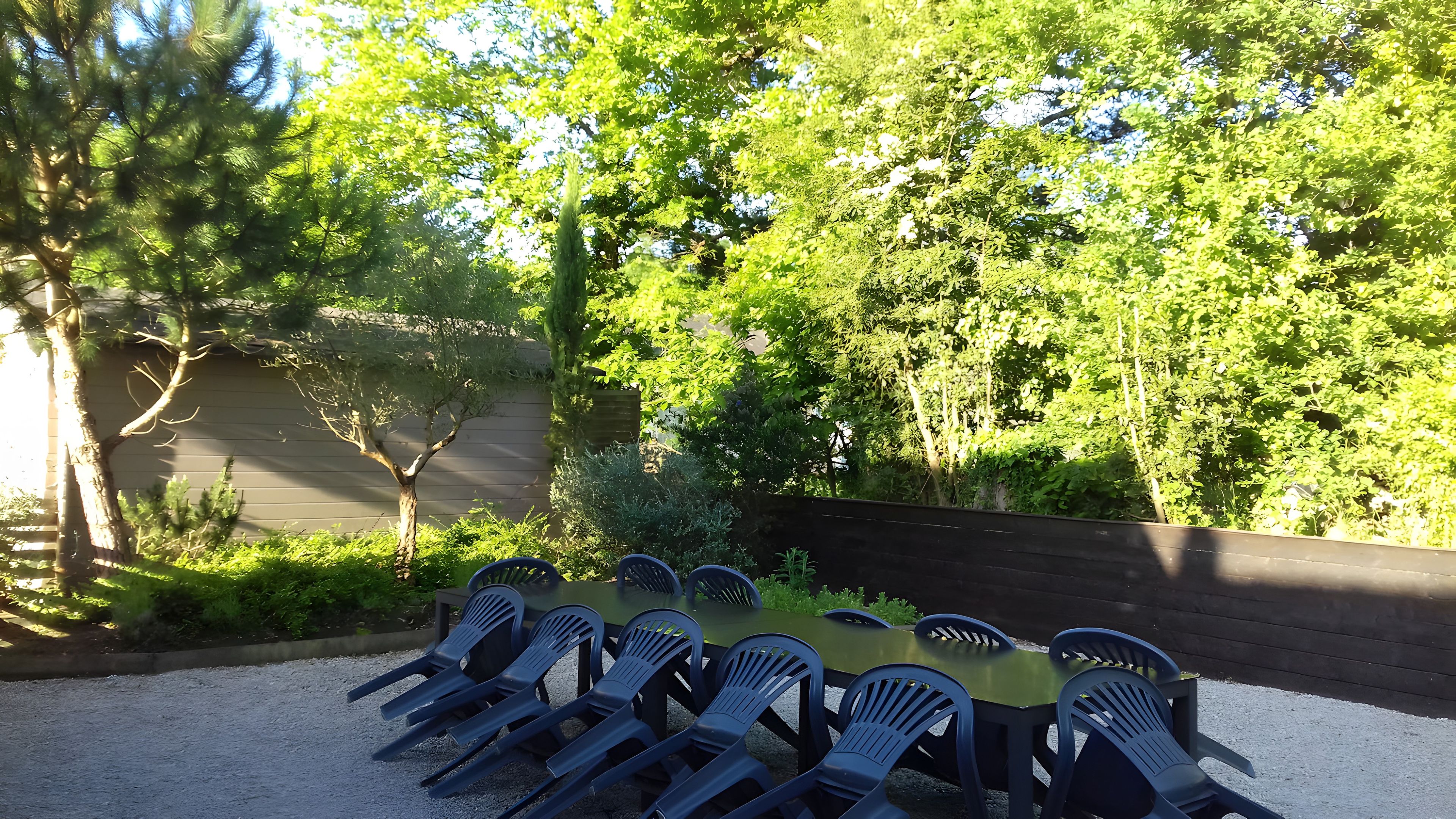 En utomhusplats med bord och stolar, omgiven av grönska och träd.