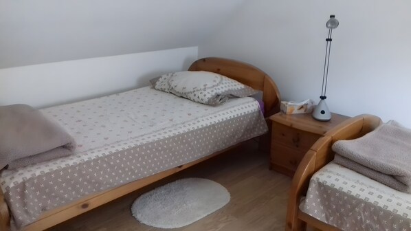En liten, välordnad säng med ett mönstrat överkast och kuddar, ett sängbord med en lampa och en stol med en kudde.