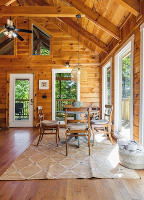 A wooden cabin interior with a dining area, chairs, a table, and a ceiling fan. - Sandstone-Cozy Cliffside Cabin, Hot Tub + Fire Pit (Stanton)
