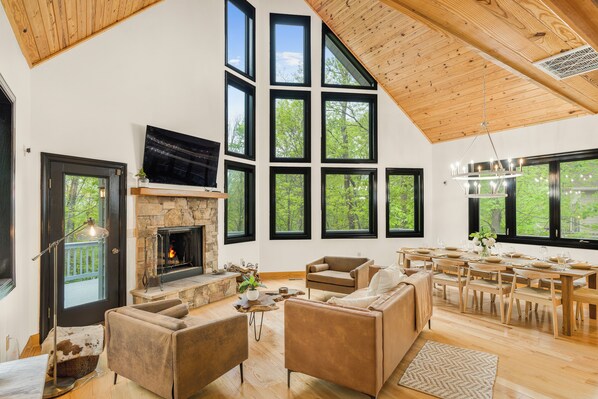 A spacious living area with a fireplace, multiple seating options, and large windows offering views of the outdoors. - Wintergreen 5BR w/ Hot Tub, Sauna, Firepit (Wintergreen Resort)
