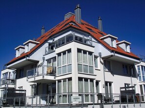 A modern building with a red-tiled roof, multiple balconies, and large windows. - Sun Deck 35 - Penthouse (Grossenbrode)