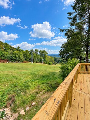 Eine Holzterrasse mit freiem Blick auf ein Wiesenfeld und Bäume.