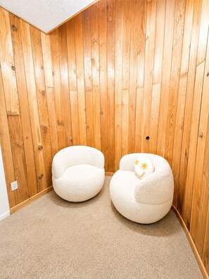 A room with wooden panel walls, two white armchairs, and a carpeted floor. - Beech Haven | Ski-In/Out • Sauna • Sleeps 18 (Beech Mountain)