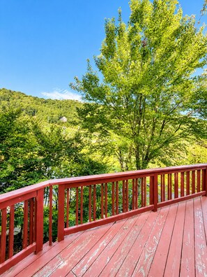 A wooden deck with a red railing overlooking a lush green landscape with trees and a hill in the background. - Beech Haven | Ski-In/Out • Sauna • Sleeps 18 (Beech Mountain)