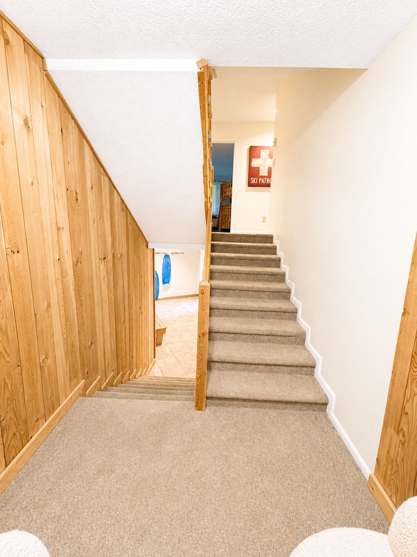 A carpeted staircase with wooden handrails leading to a room with a ski patrol sign. - Beech Haven | Ski-In/Out • Sauna • Sleeps 18 (Beech Mountain)