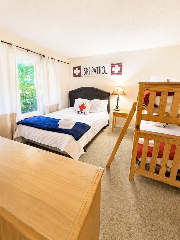 A hotel room with a bed, a wooden desk, a nightstand, a lamp, and a crib. - Beech Haven | Ski-In/Out • Sauna • Sleeps 18 (Beech Mountain)