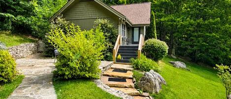 A stone pathway leading to a small wooden cabin with a porch and steps.