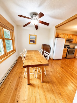 A dining area with a wooden table and chairs, a ceiling fan, a refrigerator, and wooden cabinets in a kitchen. - Tranquility House | Hot Tub • Views • Fireplace (Banner Elk)