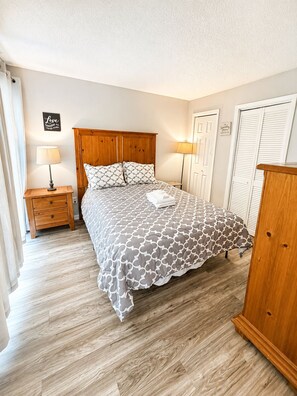 A bedroom with a wooden bed frame, a patterned bedspread, a bedside table with a lamp, and a wardrobe. - Powder Pad | Walk to Slopes • Fireplace • Deck (Beech Mountain)