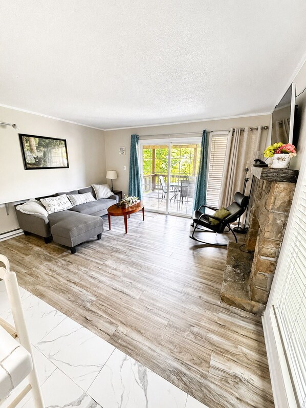 A living room with a sofa, a coffee table, a fireplace, and a view of the outdoors. - Powder Pad | Walk to Slopes • Fireplace • Deck (Beech Mountain)