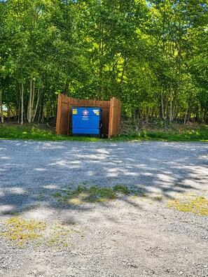 A blue dumpster with a logo, surrounded by a wooden fence, in a gravel area with trees in the background. - Powder Pad | Walk to Slopes • Fireplace • Deck (Beech Mountain)