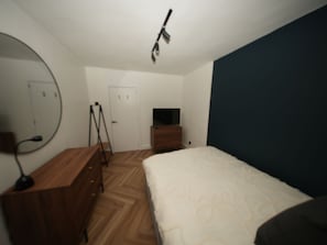 Ein Schlafzimmer mit einem Bett, einem Schminktisch, einem Spiegel und einem Fernseher auf einem Schrank.