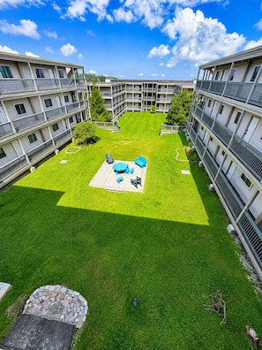 A courtyard with a grassy area, a wooden deck with outdoor furniture, and a multi-story building with balconies. - Pinnacle Inn 3302 | Views | Shared pool & hot tub (Beech Mountain)
