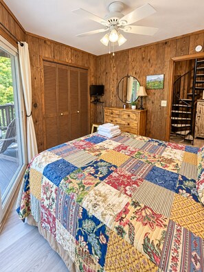 A bedroom with a large bed, wooden walls, a ceiling fan, a TV, a dresser, and a view of the outdoors. - Beech Nutz - mountain view, deck and wood burning fireplace (Beech Mountain)