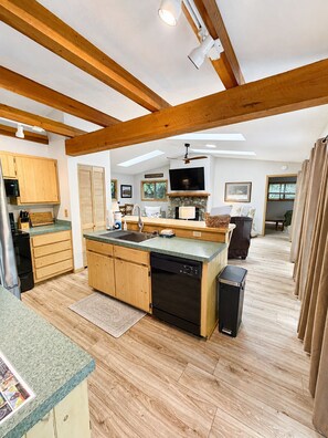 A spacious kitchen with wooden beams, a central island, and a stone fireplace. - Happy Ours - Fire Pit, Deck, Community Pool (Summertime) (Banner Elk)