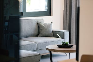Sala de estar moderna com um sofá cinzento, uma mesa de centro redonda com uma planta, e uma janela com cortinas.
