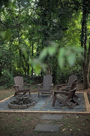 An outdoor seating area with three Adirondack chairs and a fire pit. - Cozy Camp Greene Retreat | Near Uptown Charlotte (Charlotte)