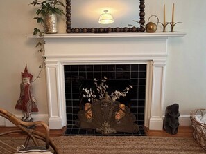 A fireplace with a decorative mantel, a wall-mounted light fixture, and a vase with branches. - Charming Historic Bungalow · Walkable to Eats/Park (Charlotte)