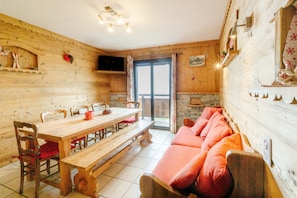 A wooden interior with a dining table, benches, a sofa, and a television mounted on the wall. - Apartment 'Sabots De Vénus' with Mountain View and Balcony (Fontcouverte-la-Toussuire)