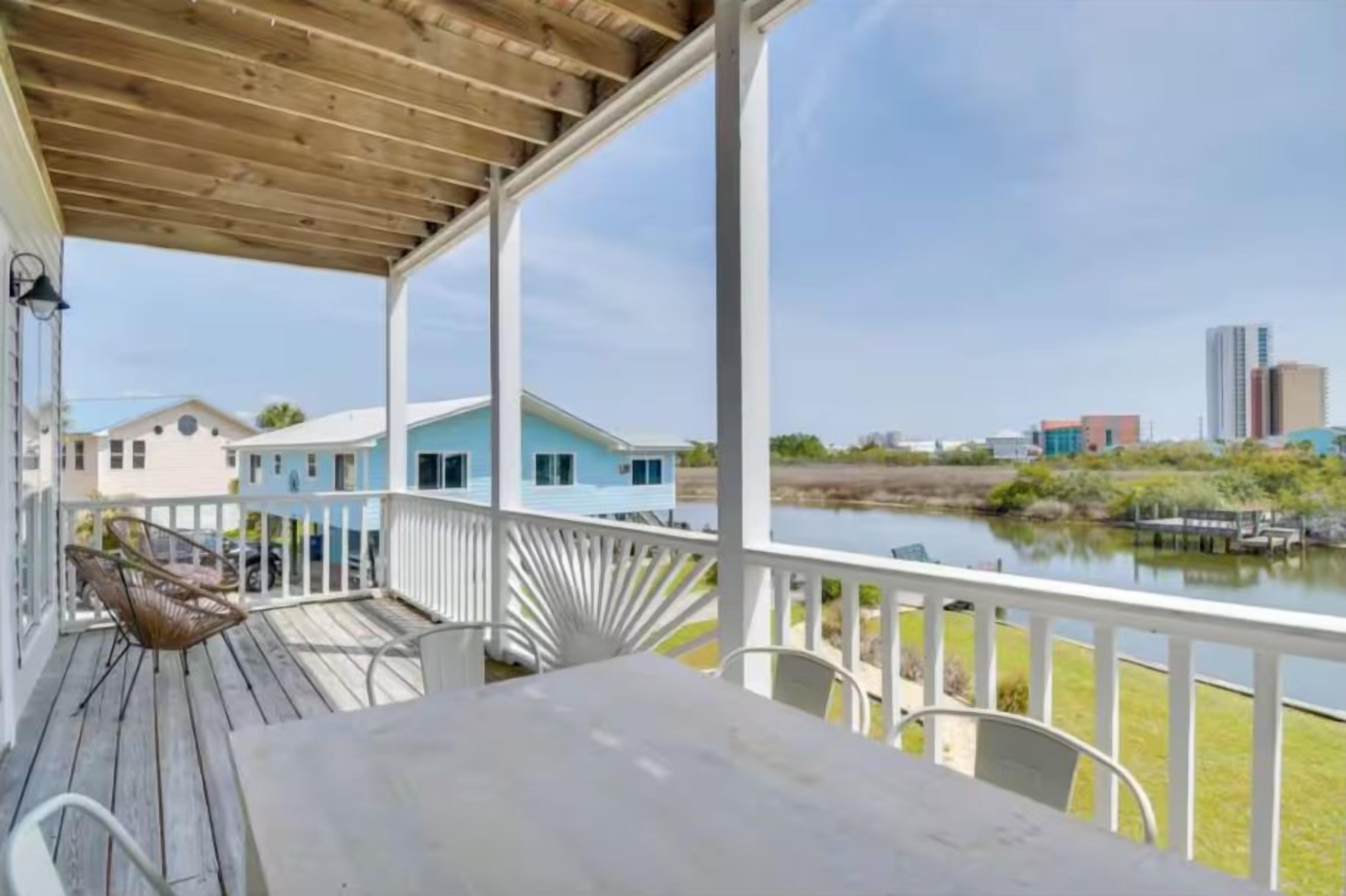 A covered outdoor area with a table and chairs, overlooking a body of water and buildings.