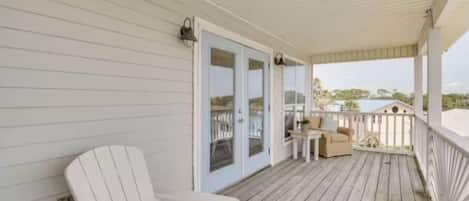 A covered porch with a white chair, a small table, and a sofa.