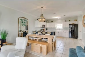 A modern kitchen with white cabinets, a dining area with a wooden table and chairs, and a large mirror with a motivational quote. - The Jungle House in Gulf Shores (Gulf Shores)