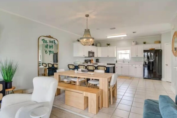Een moderne keuken met witte kasten, een eethoek met een houten tafel en stoelen, en een grote spiegel met een motiverende quote.