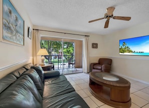 Spacious living room featuring a dark leather sofa, a wall-mounted TV, and sliding glass doors leading to a private balcony. - Sunny Isles Condo w/ Pool & Balcony, Walk to Beach (Sunny Isles Beach)