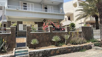 Un edificio de varios pisos con balcones, un muro de piedra y una variedad de plantas.