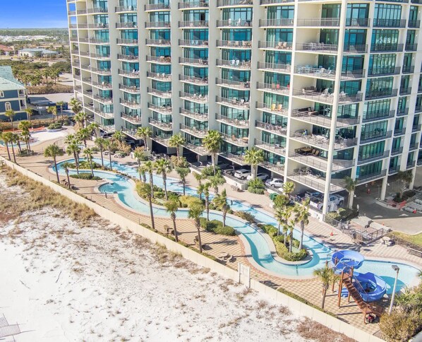 A high-rise hotel with multiple balconies, a swimming pool area, and a beach view. - Phoenix West 2502 Beachfront Bliss with Lazy River (Orange Beach)