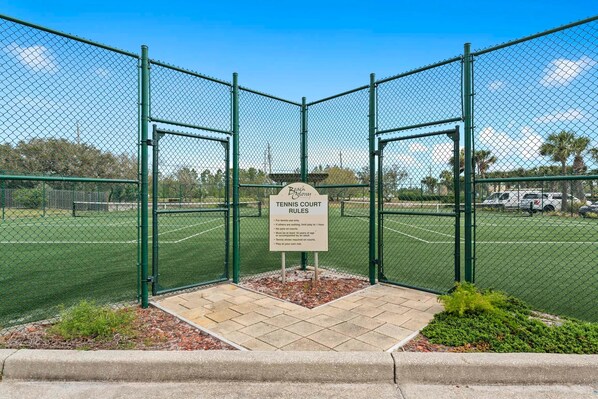 A fenced tennis court with a sign detailing court rules. - Beach Colony East 1A (Pensacola)