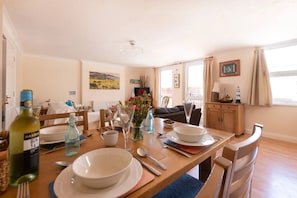 A dining area with a table set for four, a bottle of wine, and a painting on the wall. - Devon Beach Court (Woolacombe)