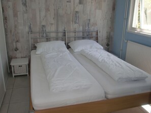 Ein Einzelzimmer mit einem Holz-Kopfteil, weißer Bettwäsche, einem kleinen Nachttisch und einem Heizkörper.