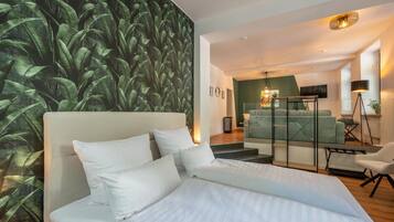 A modern bedroom with a large bed, a green accent wall, and a view into the living area.