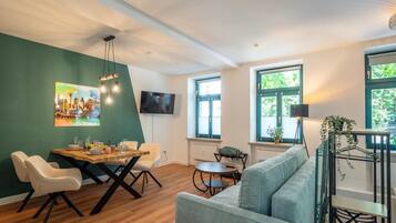 A modern living room with a dining area, a sofa, a TV, and a painting on the wall.