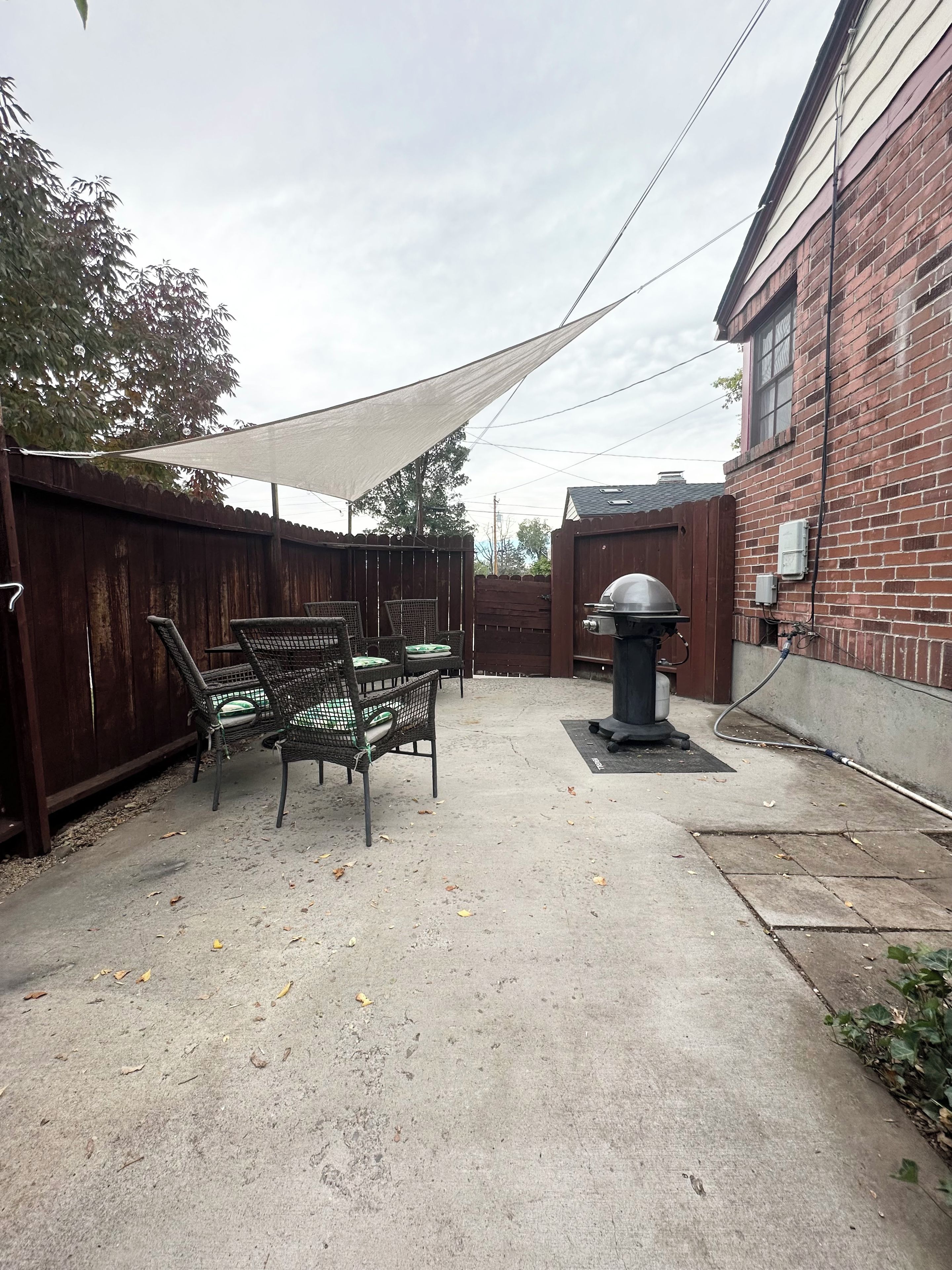 Un patio trasero con una parrilla, mobiliario exterior y una zona con sombra.