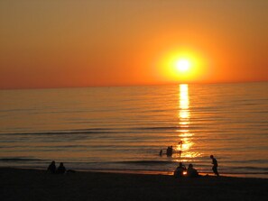 Ein Sonnenuntergang über einem ruhigen Meer mit Silhouetten von Menschen am Strand.