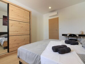 Ein Schlafzimmer mit einem Bett, einem Holzschrank, einem Schreibtisch mit Stuhl und einer Klimaanlage.