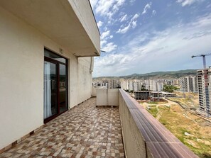 Un balcon doté d’un sol carrelé, d’une porte vitrée et offrant une vue sur le paysage urbain, avec ses bâtiments et ses chantiers de construction.