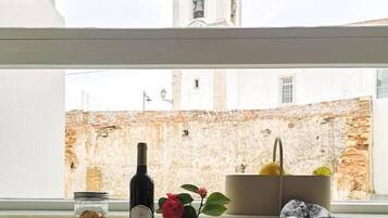 A window view of a historic building with a bell tower, a bottle of wine, a vase with a flower, and a basket with a cloth.