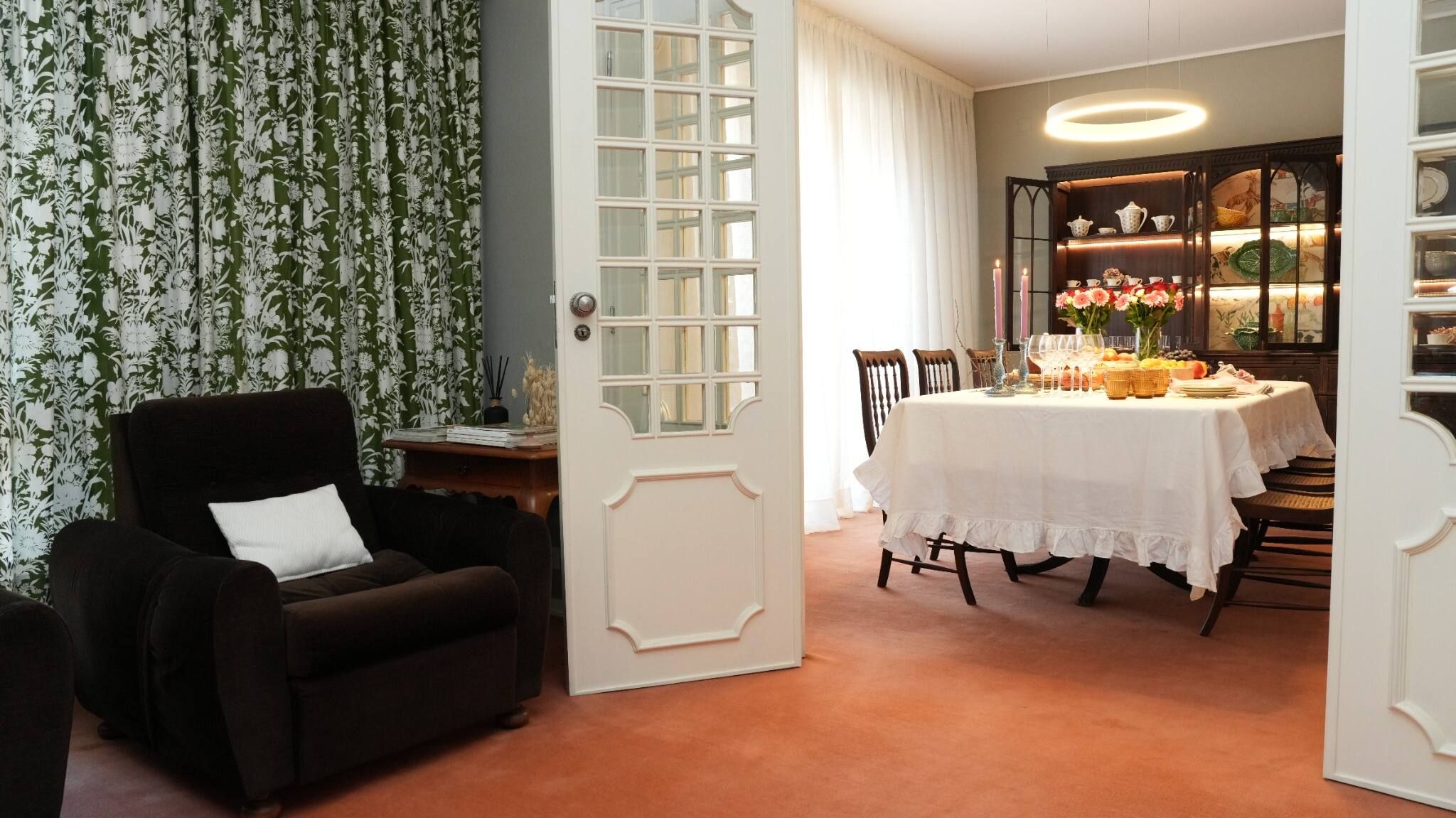 Una habitación con una mesa de comedor dispuesta para una comida, un sillón negro y una puerta con ventanal.
