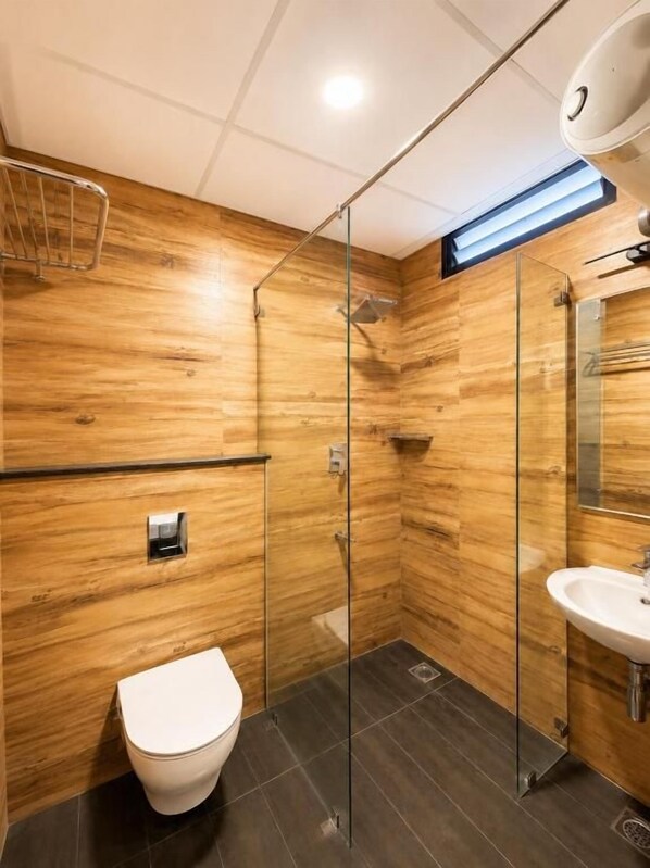 Un baño moderno con pared de madera, cabina de ducha de vidrio, inodoro blanco y lavamanos.