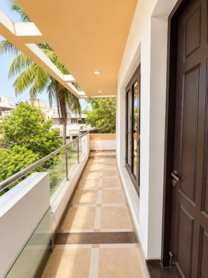 A corridor with a glass railing, a brown door, and a view of greenery outside. - JS Pleasant Stay at Nungambakkam (Chennai)