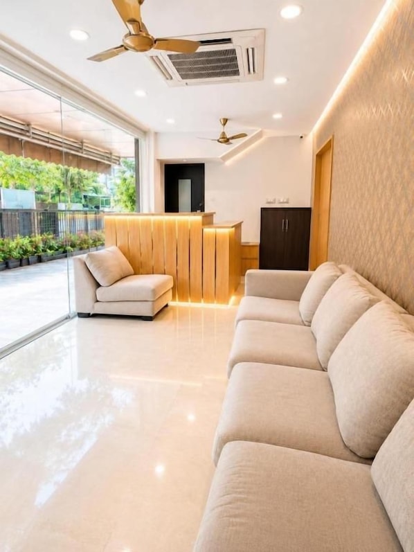 A modern hotel lobby with a reception desk, a sofa, and a ceiling fan. - JS Pleasant Stay at Nungambakkam (Chennai)