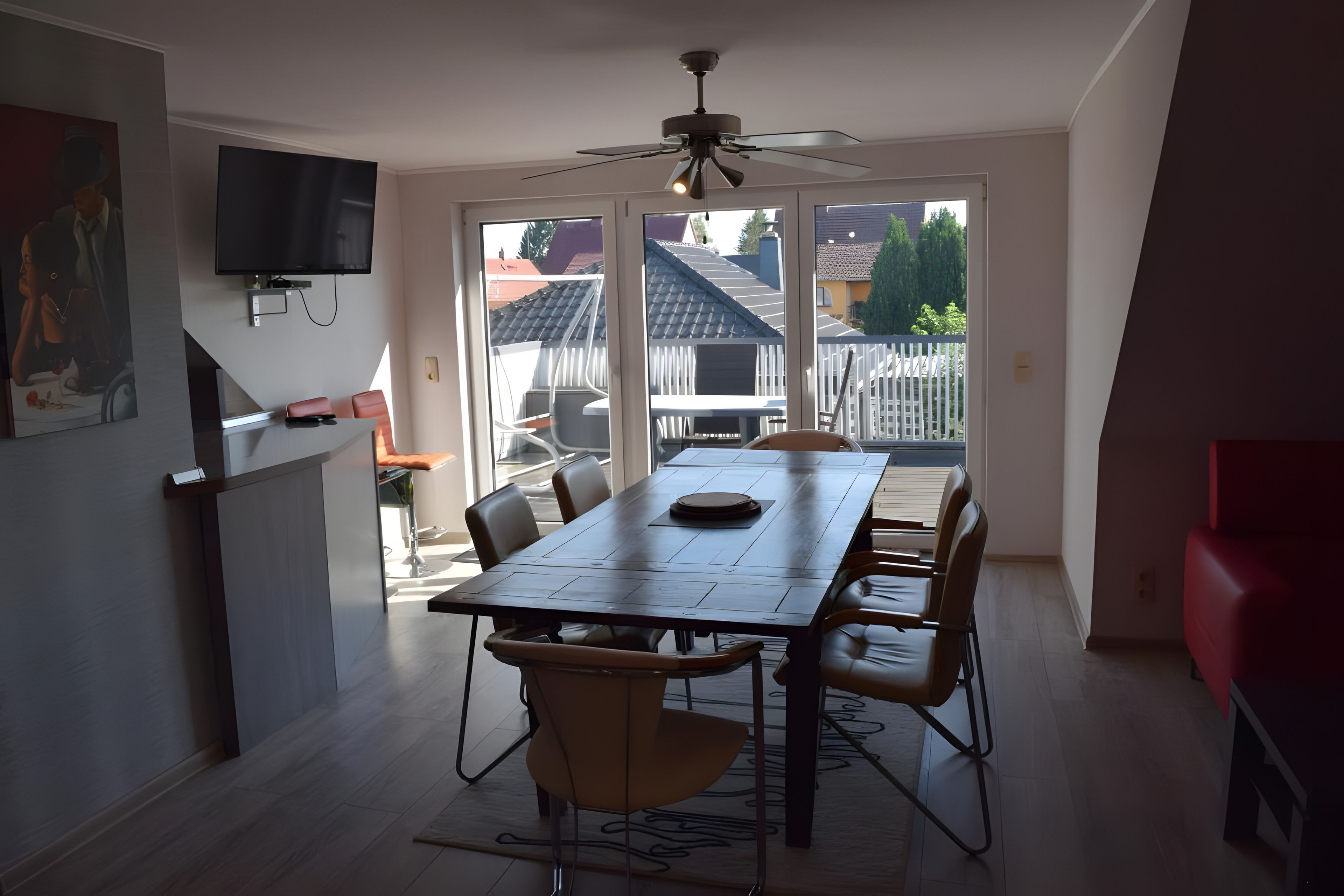 Ein Essbereich mit Tisch und Stühlen, einem Deckenventilator und einem an der Wand befestigten Fernseher.